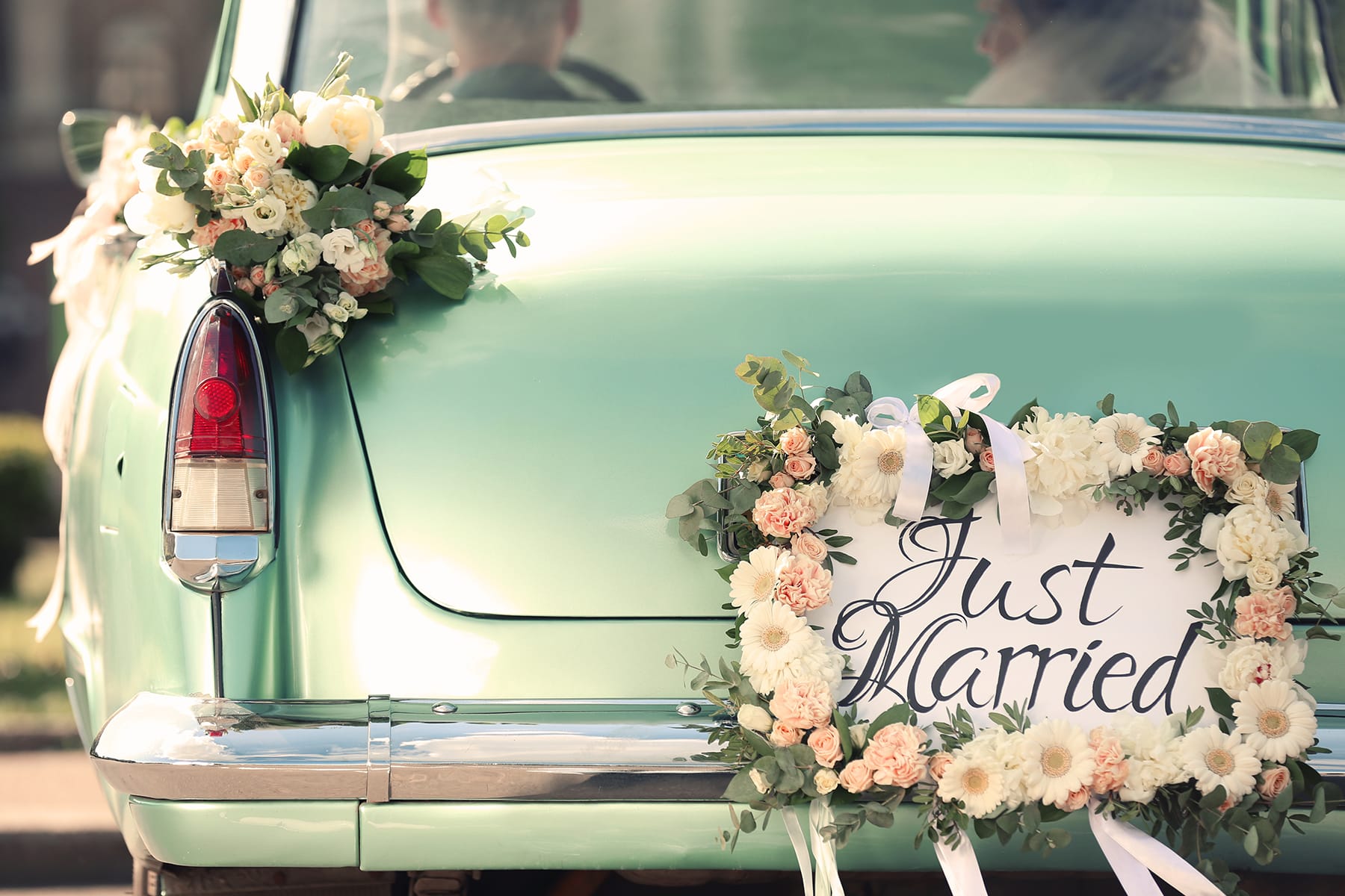 Mint-green vintage car decorated with white and pink flowers for a wedding, featuring a 'Just Married' banner on the trunk.