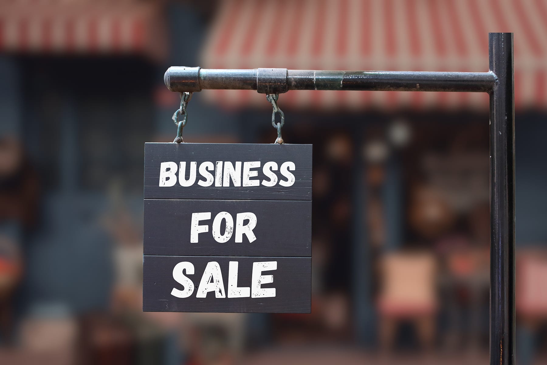 Dark wooden sign reading 'BUSINESS FOR SALE' hanging from a metal pipe.