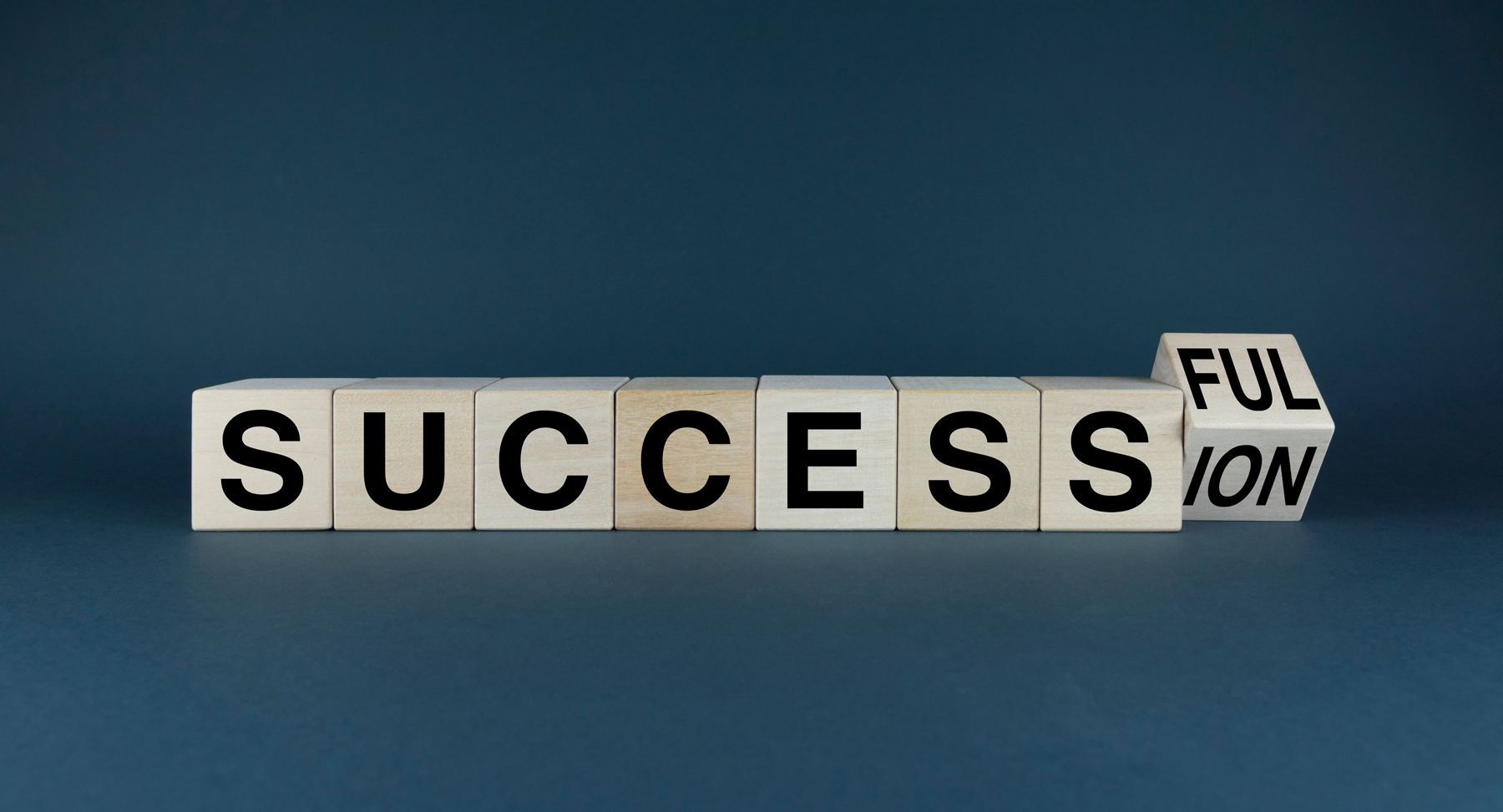 Wooden letter blocks spell 'SUCCESS' in a row, with a final split block showing 'FUL' and 'TION' to hint at 'successful'.