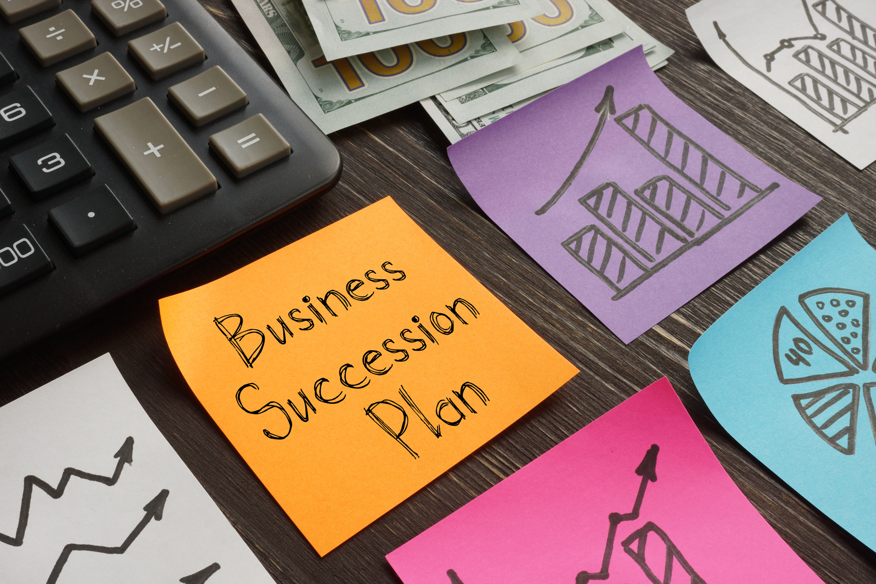 Orange note reads 'Business Success Plan' beside a calculator and money, on a wooden desk with colorful sketches and charts.